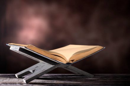 Quran open in wooden placemat on wooden table over blurry background