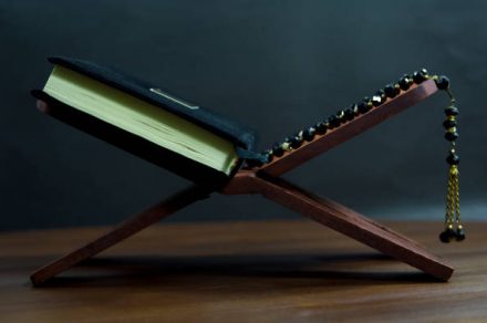 closeup of Islamic Muslims holy Book Quran with wooden stand and paternoster Tasbeeh on a wood table and black background